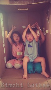 LP and his sisters in a large cardboard box, all doing the ASL sign for "shark" as part of the Slippery Fish song. LP is sitting on one sister's lap only wearing a shirt and underwear.